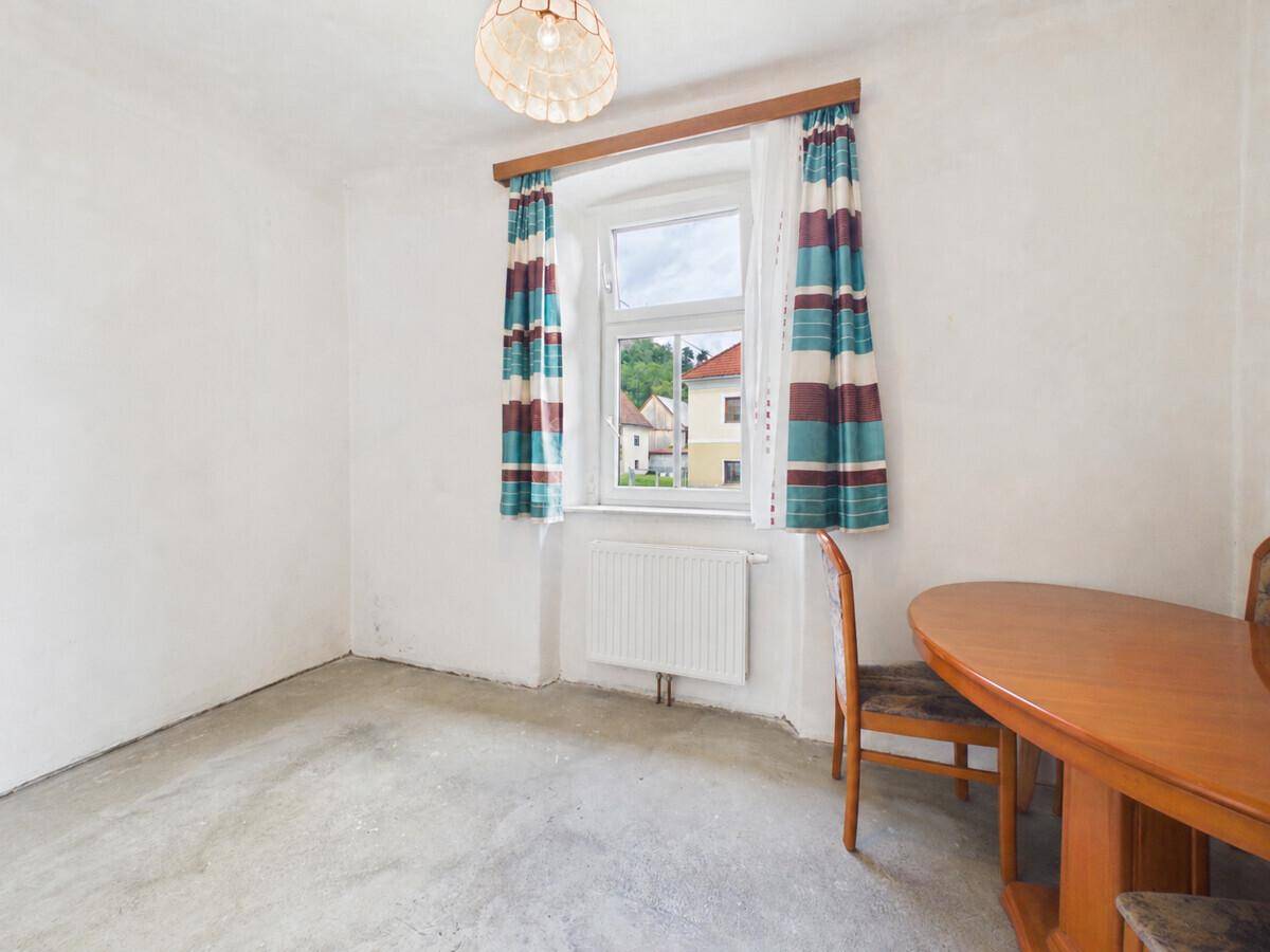 Raum mit Betonboden und einem Fenster mit gestreiften Vorhängen, bereit für die Renovierung.