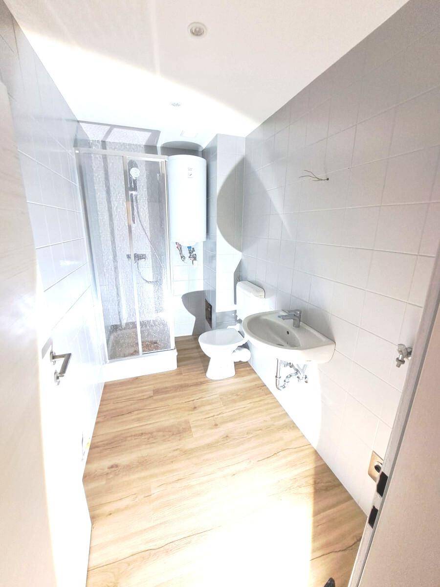 Modernes Badezimmer mit Duschkabine, WC, Waschbecken und hellen Fliesen an den Wänden.