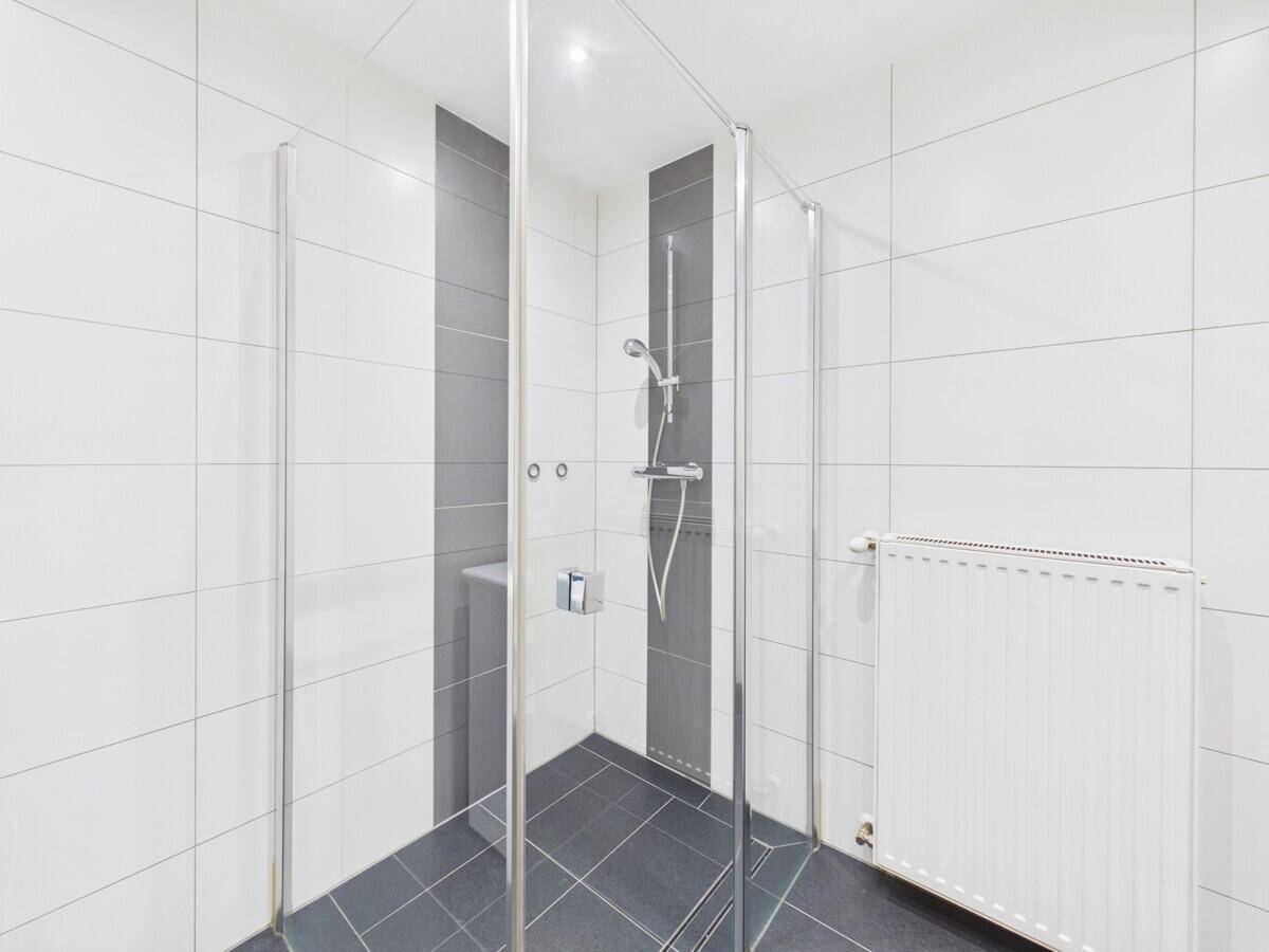 Modernes Duschbad mit Glasduschkabine, weißen Fliesen und Heizkörper.