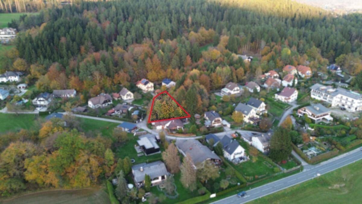 Luftaufnahme eines Wohngebiets mit Wald im Hintergrund und markiertem Grundstück in Herbstfarben.
