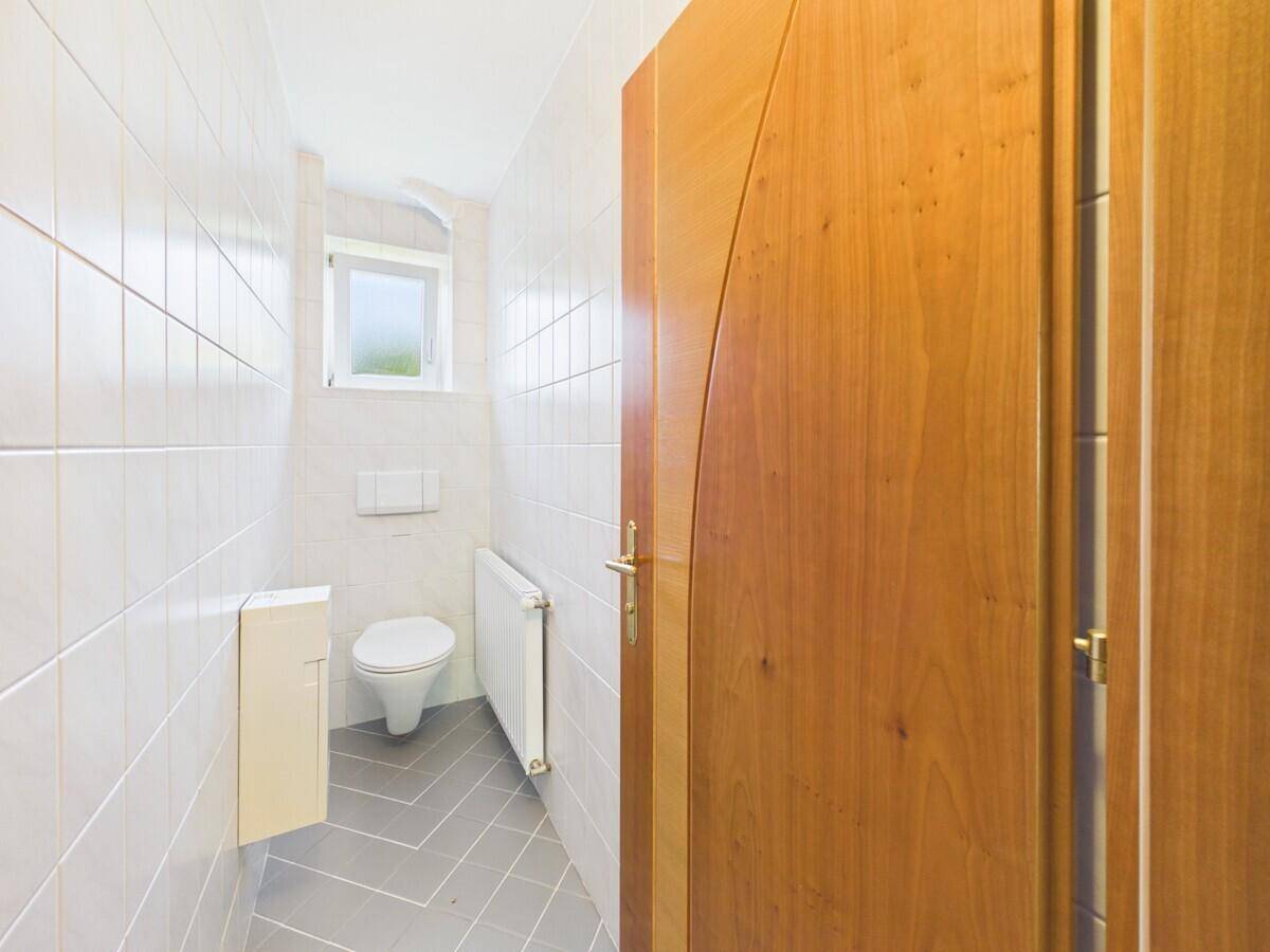 Kleines Gäste-WC mit weißen Fliesen, wandhängendem WC und Fenster.