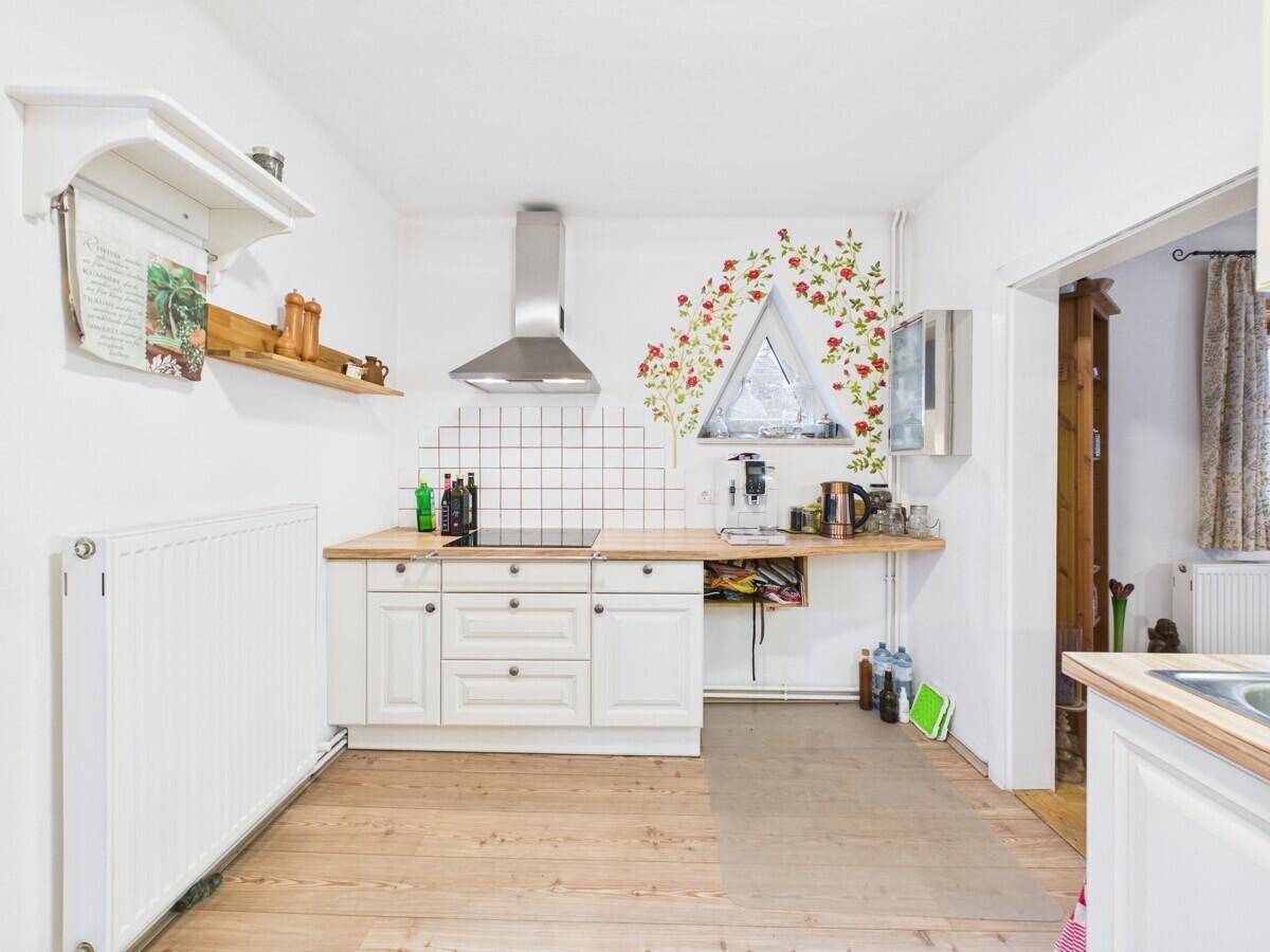 Helle Küche mit Induktionskochfeld, Dunstabzugshaube und floraler Wanddekoration.