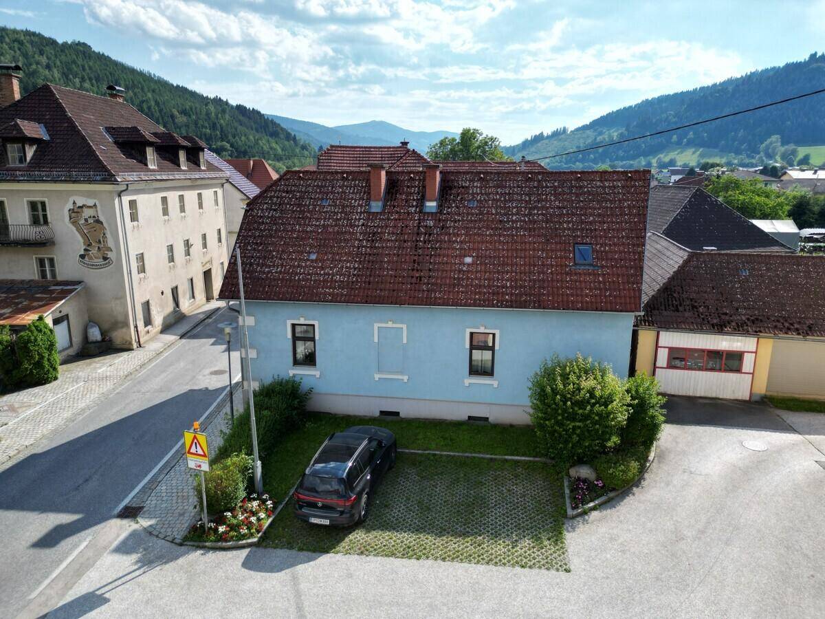 Rückansicht des Hauses mit Parkplatz, Rasenfläche und einem malerischen Bergblick im Hintergrund.