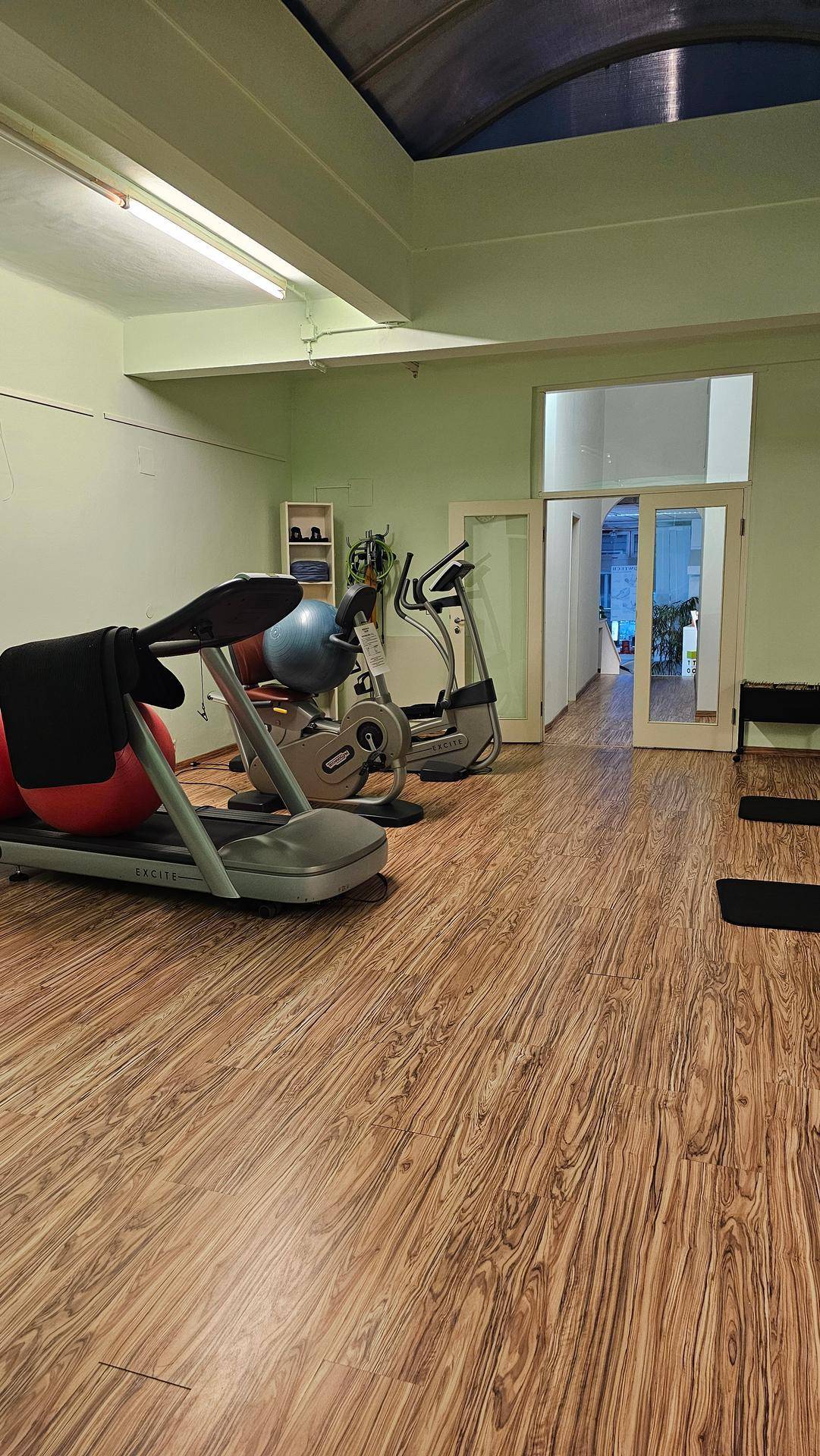 Geräumiger Fitnessbereich mit Laufbändern, Ergometern und einem hellen Holzboden, ideal für Trainingseinheiten.
