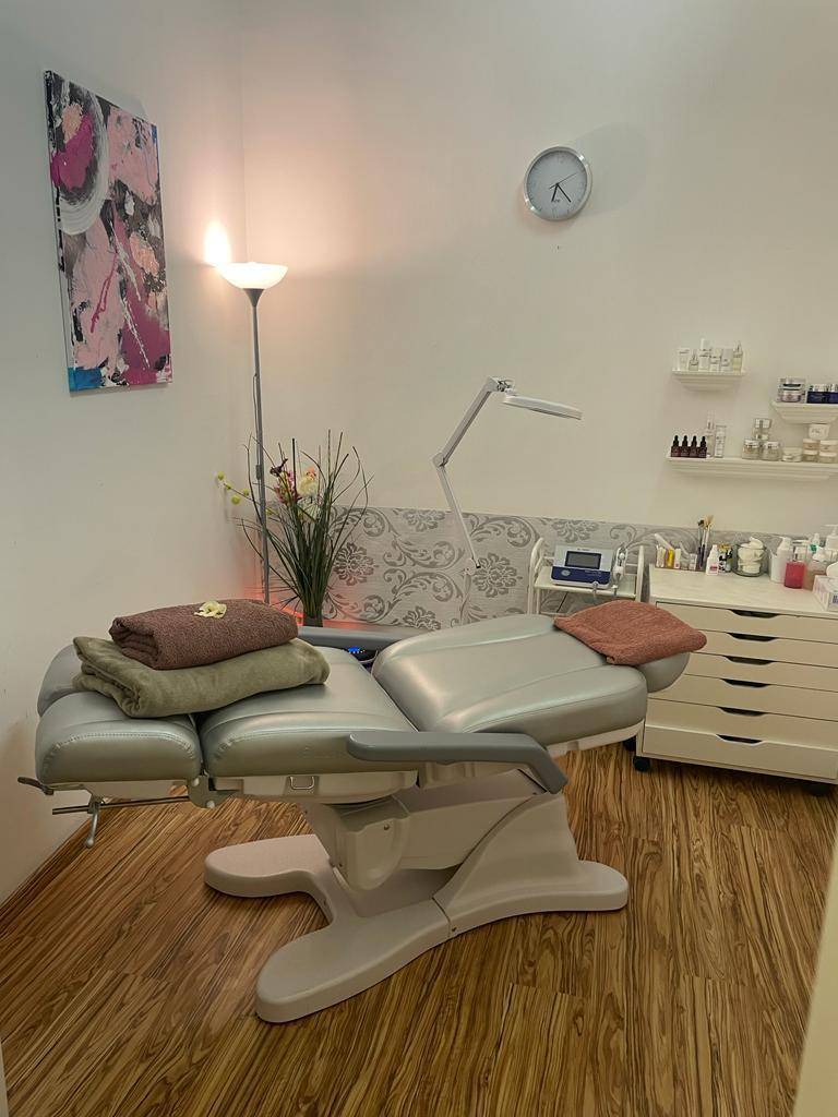 Heller Behandlungsraum mit einer komfortablen Liege, Stehlampe und Regalen für Produkte in modernem Stil.