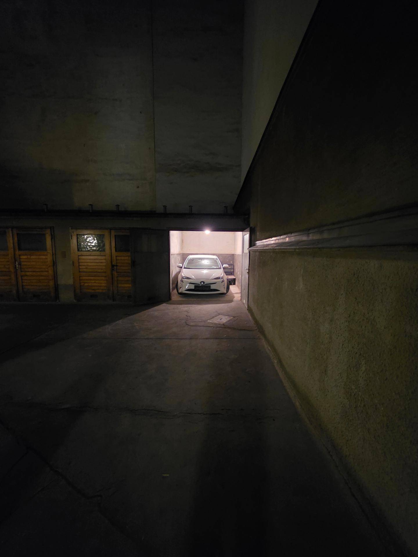 Blick in eine Garage mit einem weißen Auto im Inneren, umgeben von dunklen Wänden.