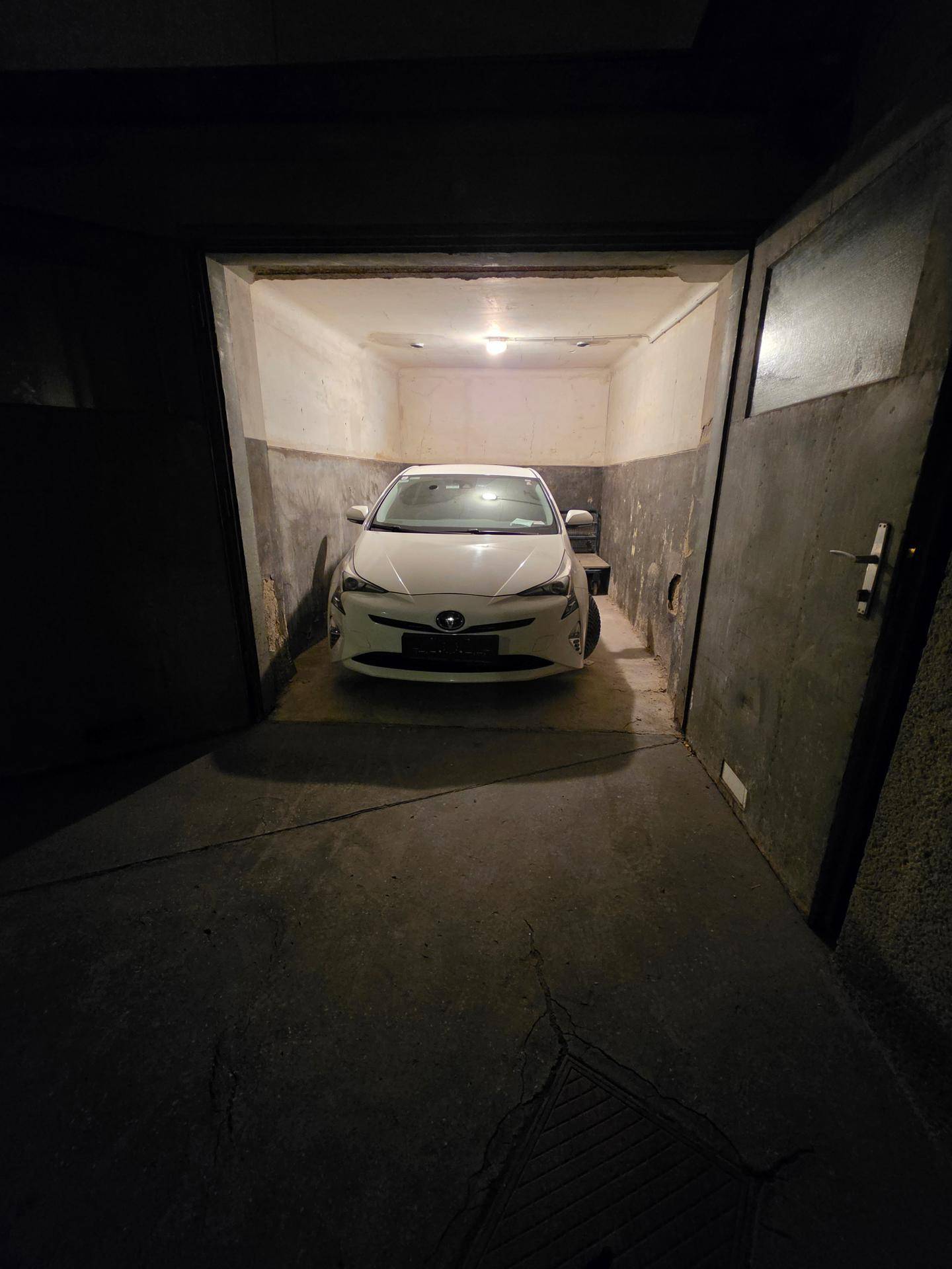Innenansicht einer Garage mit einem weißen Auto und schwacher Beleuchtung an der Decke.