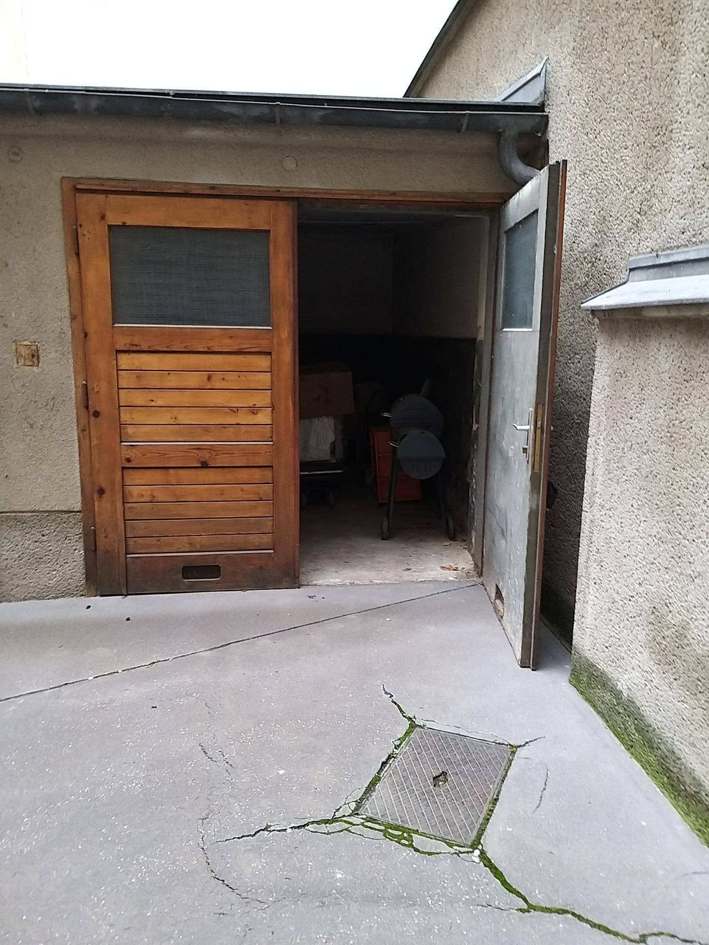 Geöffnete Holztür und Metalltür eines Garagen- oder Lagerbereichs in einem Hof mit Betonboden.