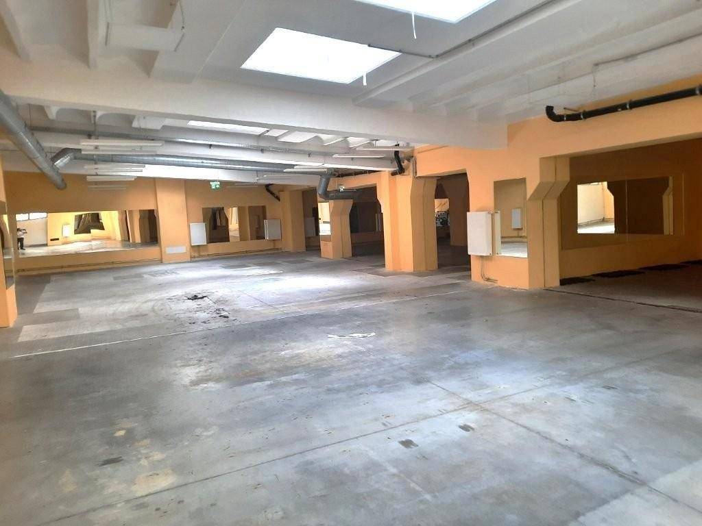 Großer, leerer Gewerberaum mit Betonboden, orangefarbenen Wänden und sichtbaren Lüftungsrohren an der Decke.