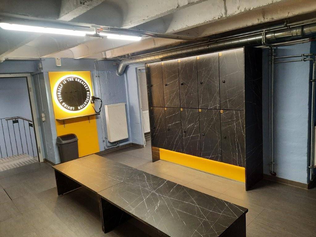 Moderner Umkleideraum mit schwarzen Spinden, einer Sitzbank und gelben Akzenten an den Wänden.