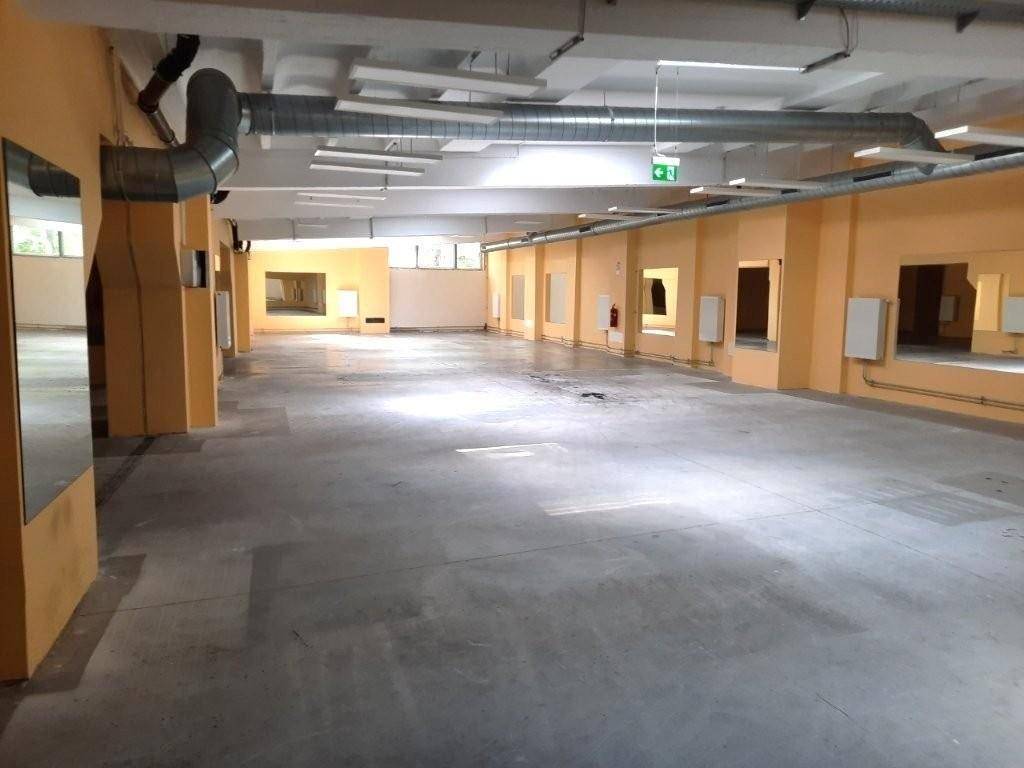 Weitläufiger Gewerberaum mit Betonboden, orangefarbenen Wänden, großen Fenstern und sichtbaren Deckeninstallationen.