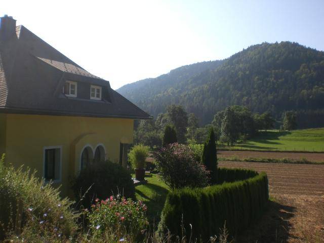 Gelbes Haus mit Blick auf weite Felder und bewaldete Hügel in ländlicher Umgebung.