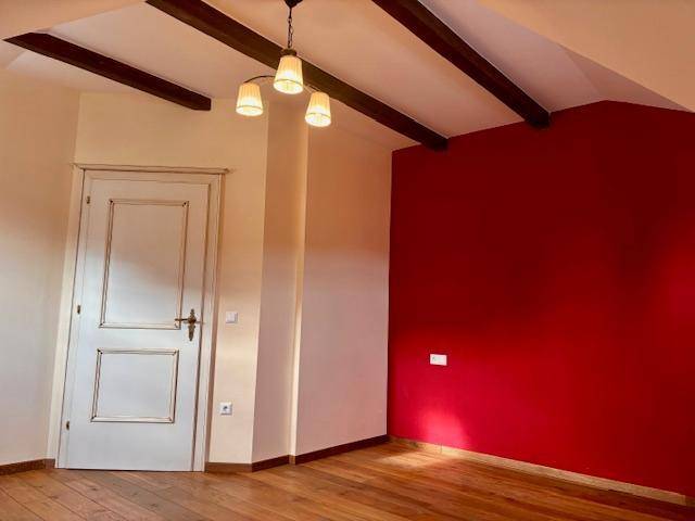 Schlafzimmer mit Holzboden, roter Akzentwand und weißer Tür, unter Dachschräge.