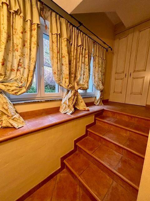 Treppenbereich mit Terrakotta-Fliesenboden, Fenster und floral gemusterten Vorhängen.