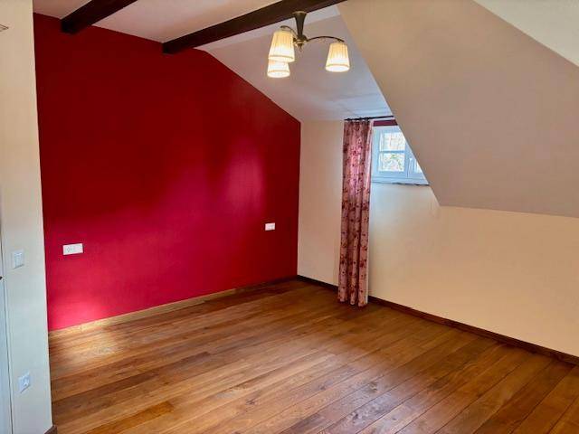 Schlafzimmer mit roter Akzentwand, Holzboden und sichtbaren Deckenbalken unter Dachschräge.