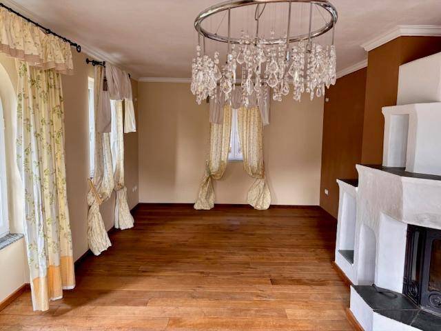 Geräumiges Wohnzimmer mit Holzboden, Kronleuchter und großen Fenstern, bereit zur Einrichtung.