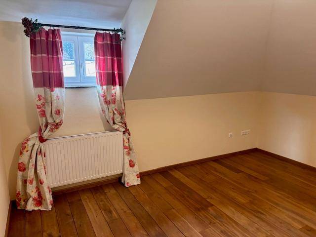 Schlafzimmer mit Holzboden und Fenster, dekoriert mit roten Vorhängen, unter Dachschräge.