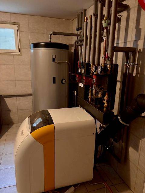 Heizungsraum mit Warmwasserspeicher, Rohrleitungen und Fliesenboden.