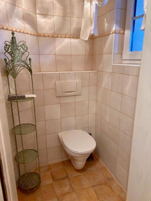 Kleines Gäste-WC mit beigefarbenen Fliesen, Toilette und einem Fenster für Tageslicht.
