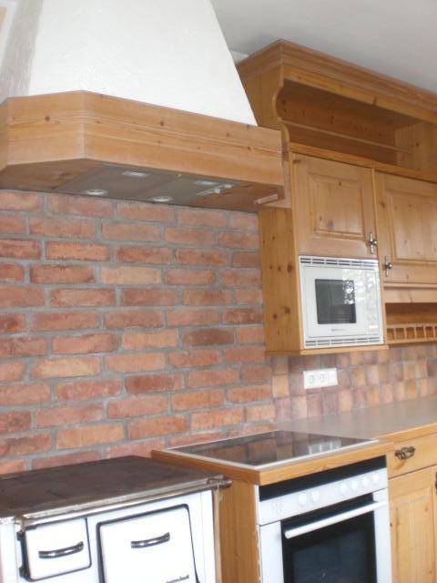 Detailansicht der traditionellen Holzküche mit Backsteinwand und integrierten Geräten.