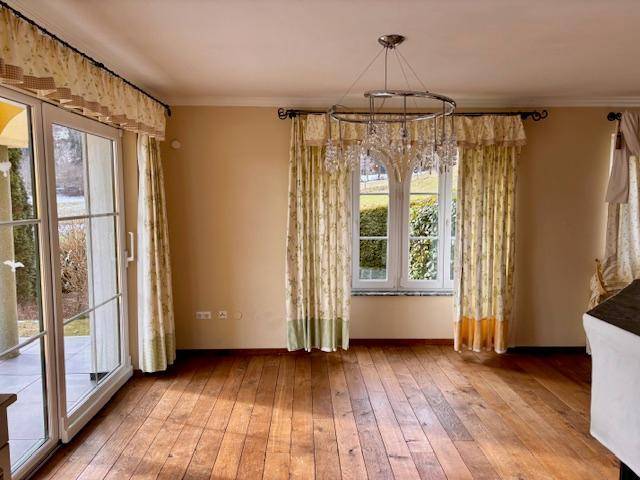 Geräumiges Wohnzimmer mit Holzboden, Kronleuchter und großen Fenstern mit Blick ins Grüne.