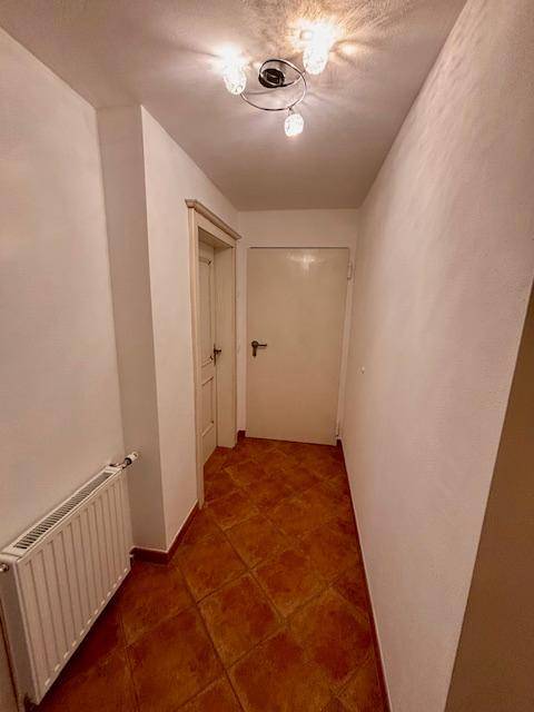 Schmaler Flur mit Terrakotta-Fliesenboden, weißen Wänden und einem Heizkörper.