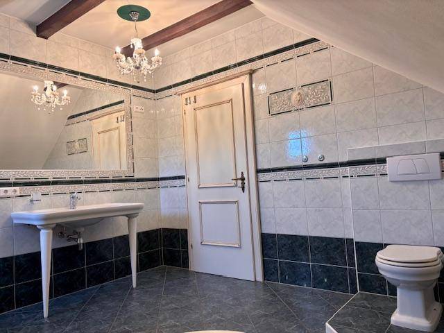 Badezimmer mit Waschtisch, Spiegel und WC, gefliest in Grün und Weiß, unter Dachschräge.