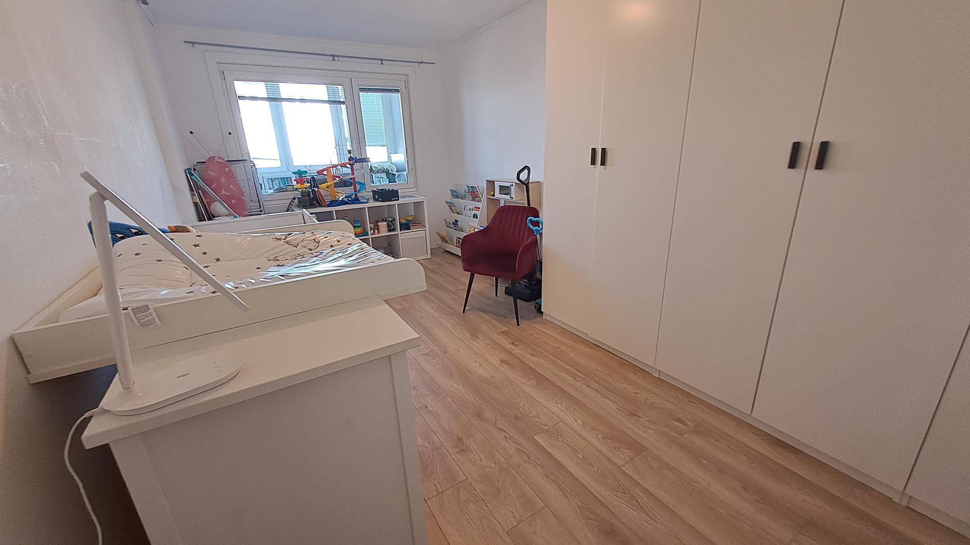 Kinderzimmer mit hellem Holzboden, großem Kleiderschrank und Spielzeugbereich.