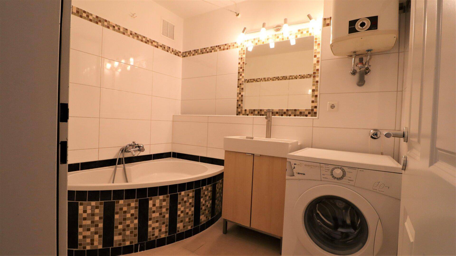Gefliestes Badezimmer mit Eckbadewanne, Waschbecken und Waschmaschine.