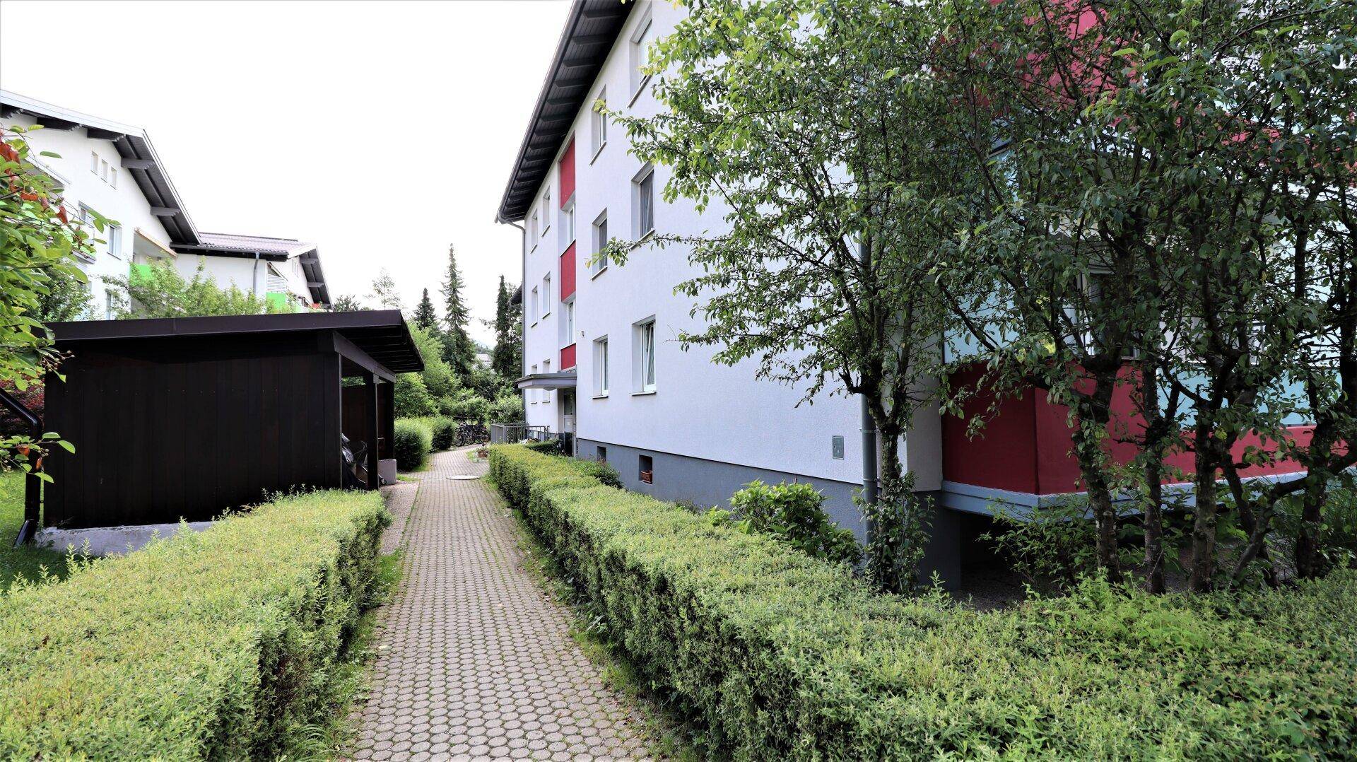 Außenansicht eines Wohngebäudes mit gepflegter Hecke und einem gepflasterten Weg.