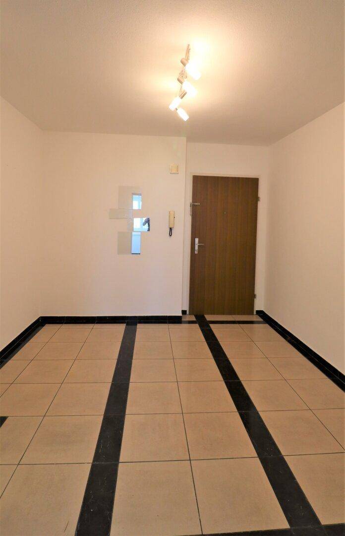 Eingangsbereich mit Fliesenboden und einer Holztür, die in die Wohnung führt.