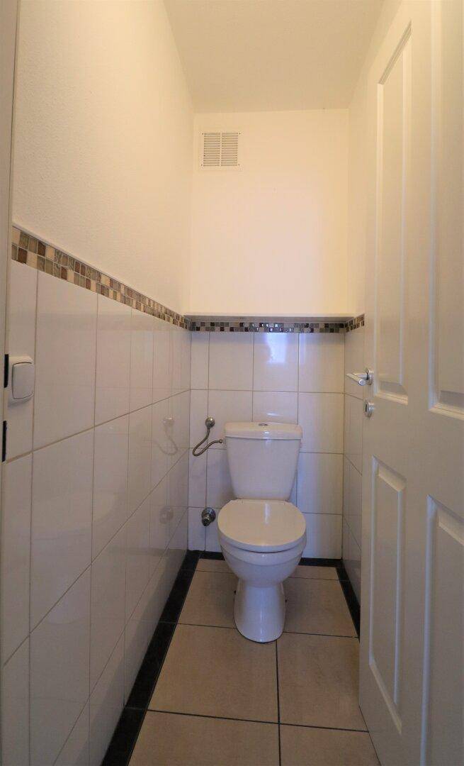 Separates WC mit weißen Fliesen und einer einfachen Toilette, funktional und sauber.
