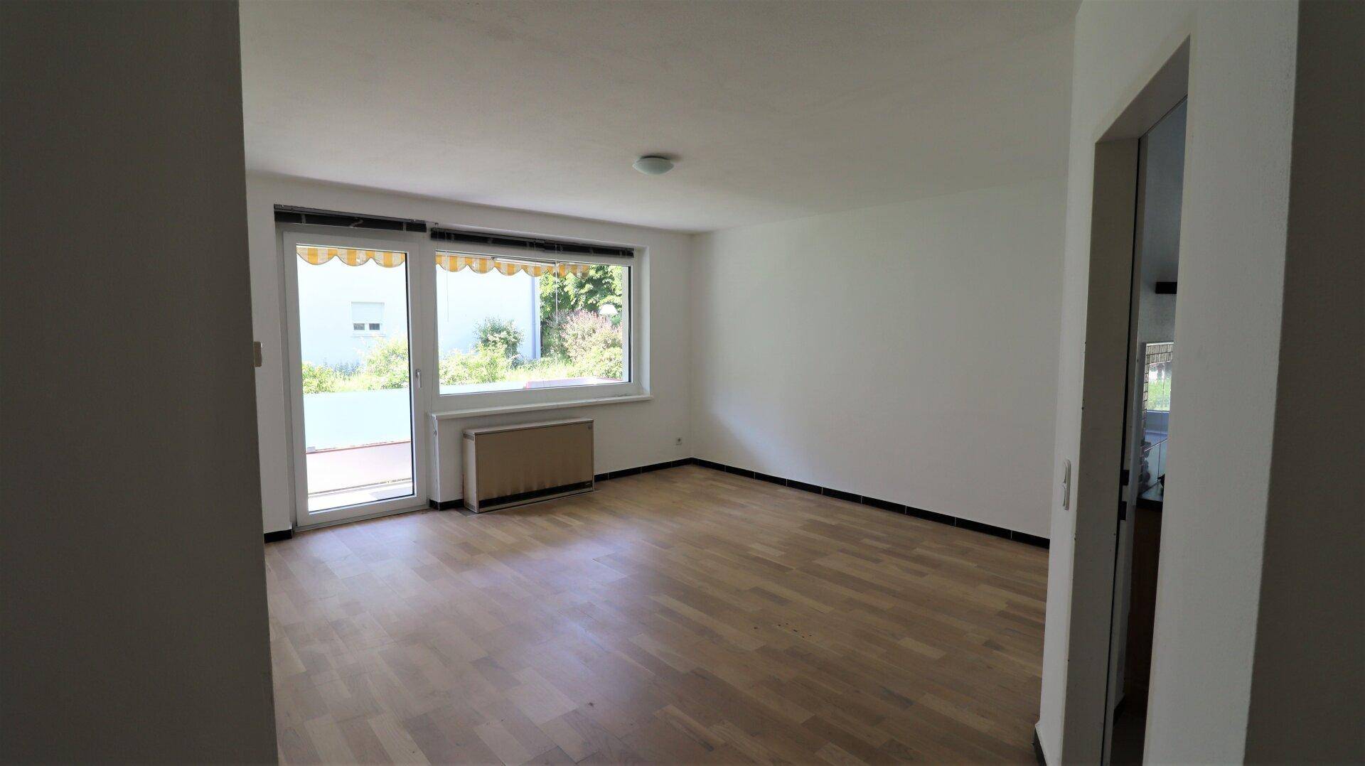 Heller Wohnraum mit Parkettboden, großem Fenster und direktem Zugang zum Balkon.