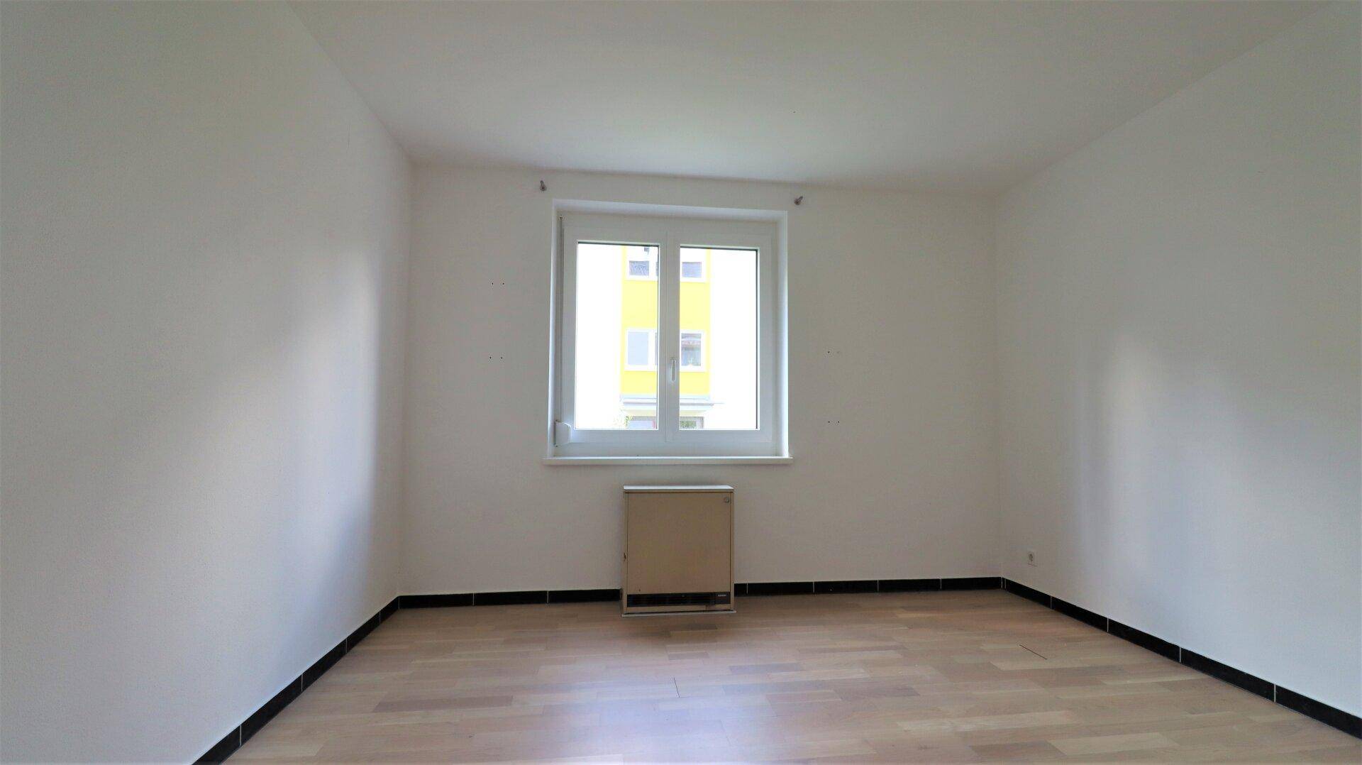 Helles Schlafzimmer mit Parkettboden und einem Fenster, das viel Tageslicht hereinlässt.