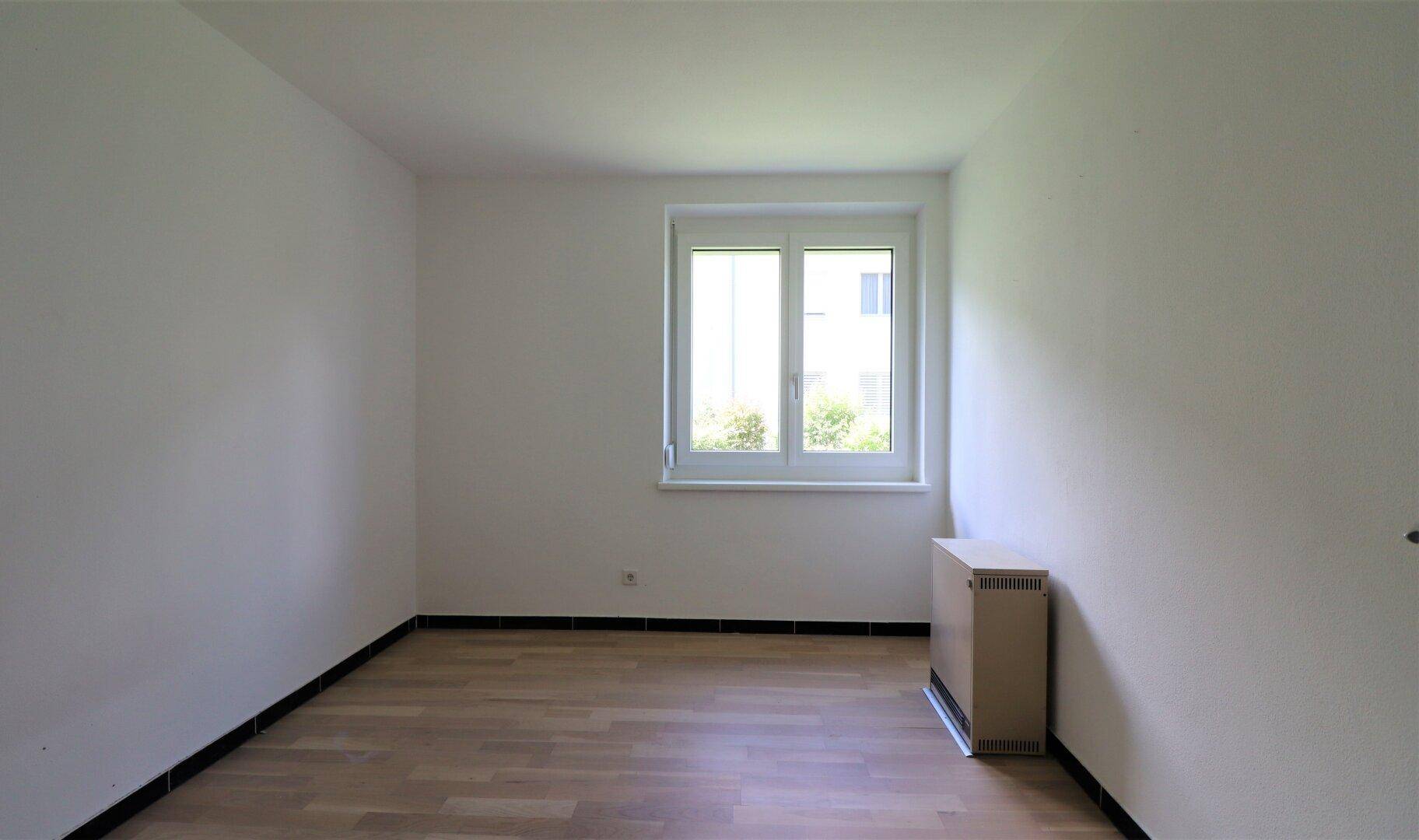 Geräumiges Schlafzimmer mit Parkettboden und einem großen Fenster, das den Raum erhellt.