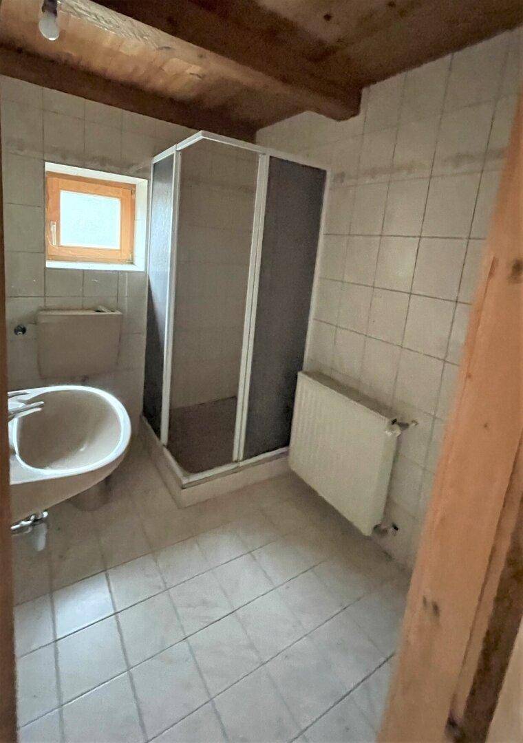Badezimmer mit Duschkabine, Waschbecken und Fenster, gefliest in Weiß.