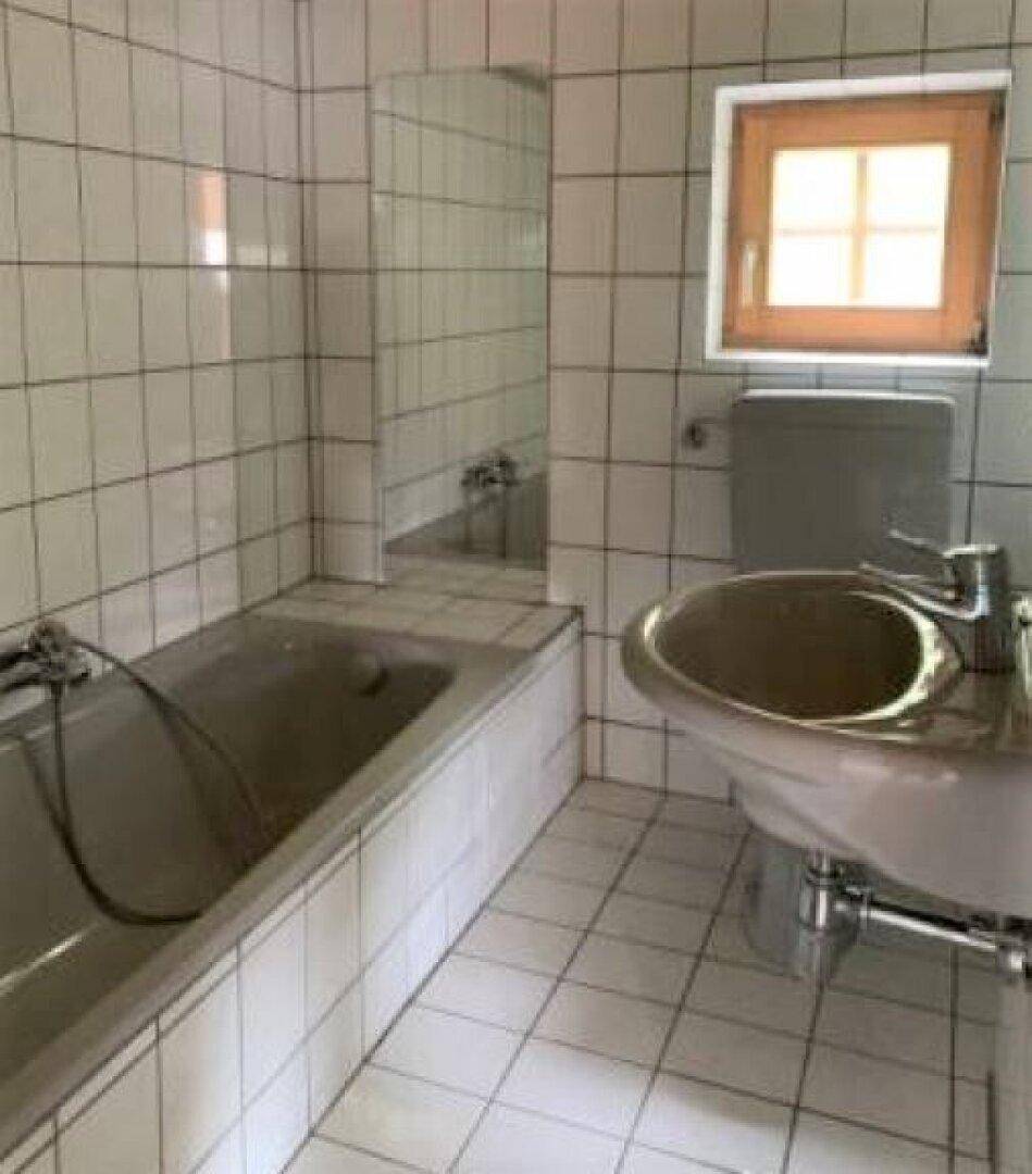 Badezimmer mit Badewanne, Waschbecken und Fenster, gefliest in Weiß.