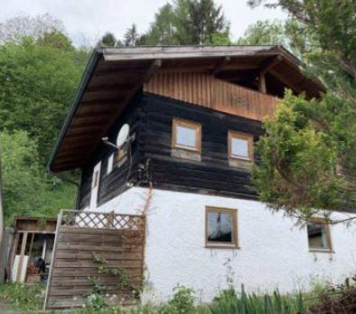 Rustikales Haus mit Holzfassade und weißem Putz, eingebettet in grüne Umgebung.
