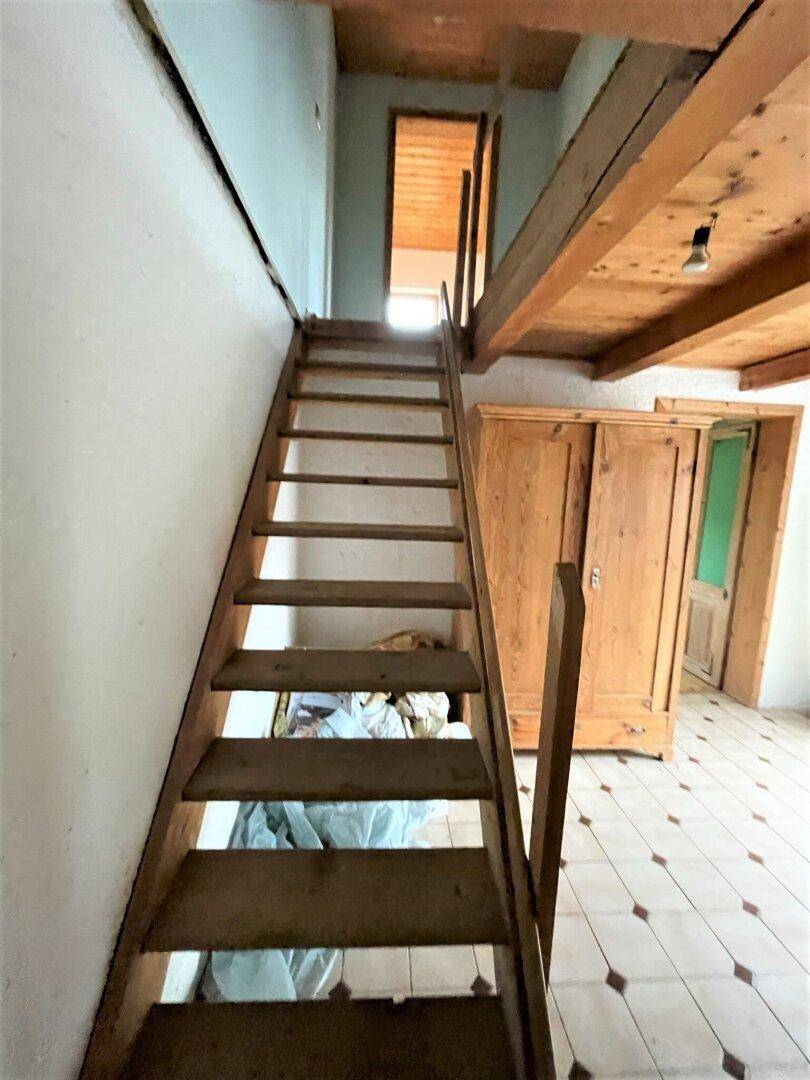 Holztreppe führt in den oberen Bereich, umgeben von rustikalen Elementen und Fliesenboden.