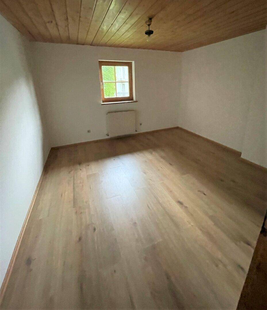 Helles Schlafzimmer mit Holzboden, Holzdecke und einem Fenster mit Blick ins Grüne.