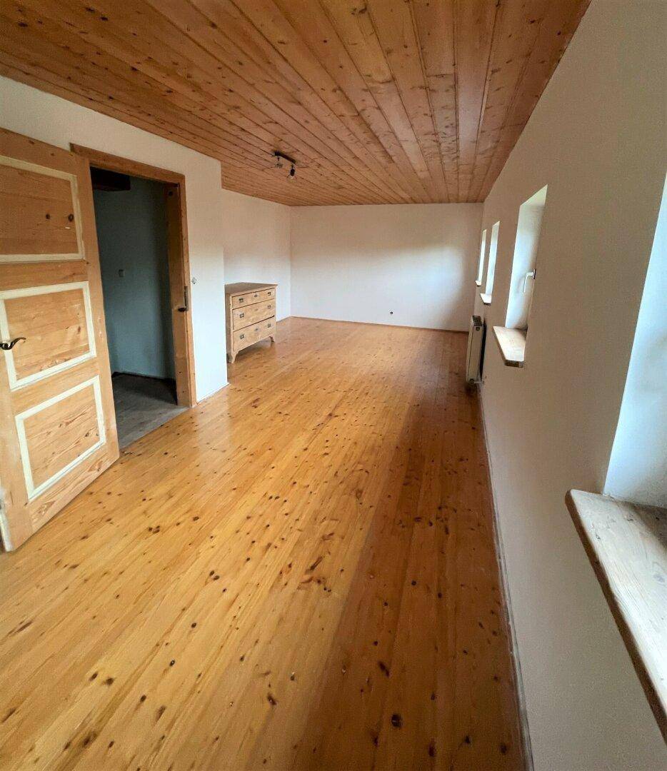 Geräumiges Zimmer mit Holzboden, Holzdecke und kleinen Fenstern, bereit zur Einrichtung.