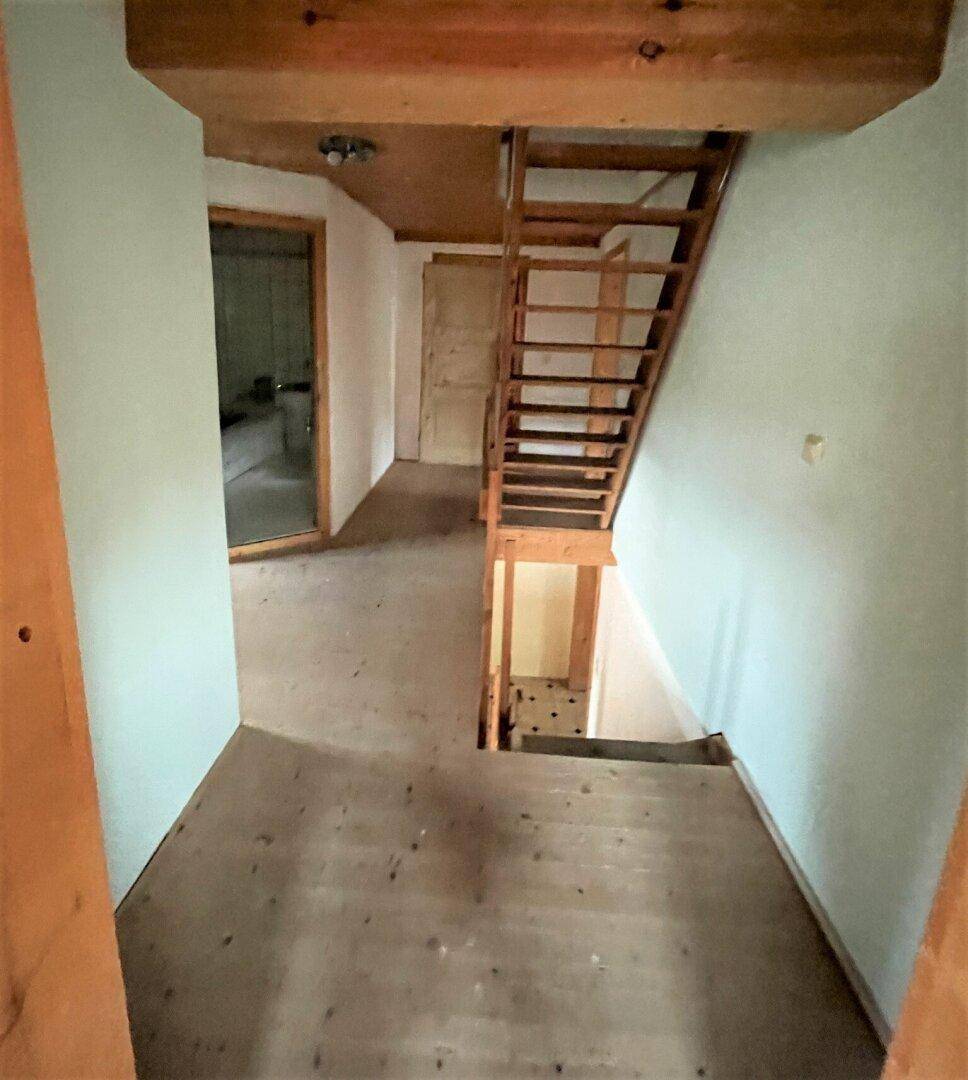 Oberer Flurbereich mit Holzbalken, Holzdecke und Blick auf die Treppe.