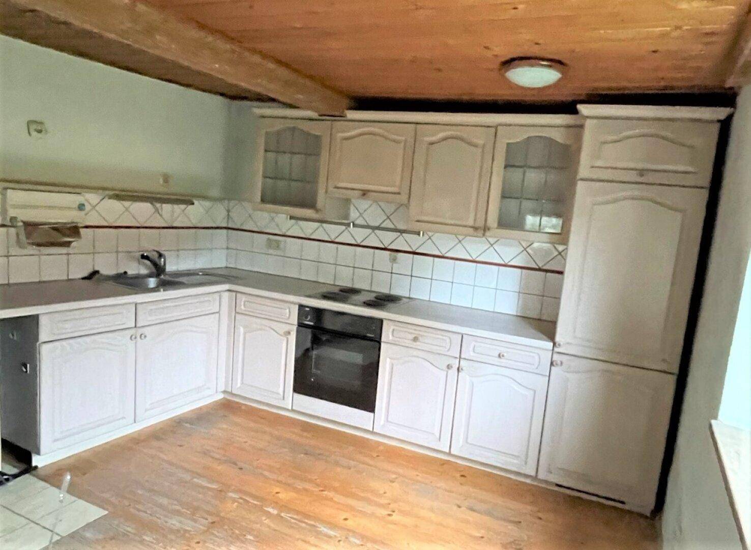 Küche mit hellen Holzschränken, Fliesenspiegel und Holzbalkendecke, bereit zur Modernisierung.