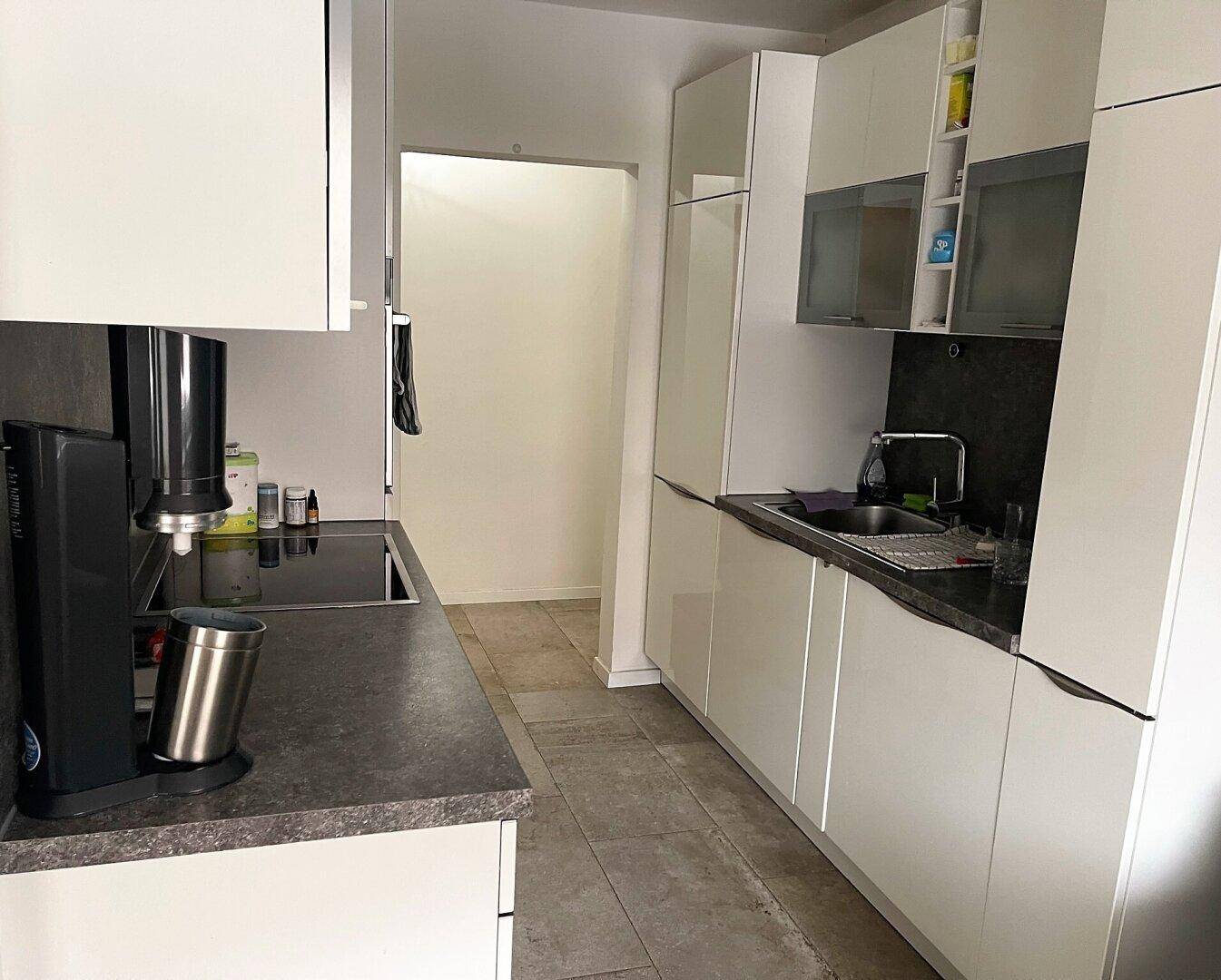 Moderne Küche mit weißen Hochglanzschränken, dunkler Arbeitsplatte und Fliesenboden, ausgestattet mit Kochfeld und Spüle.