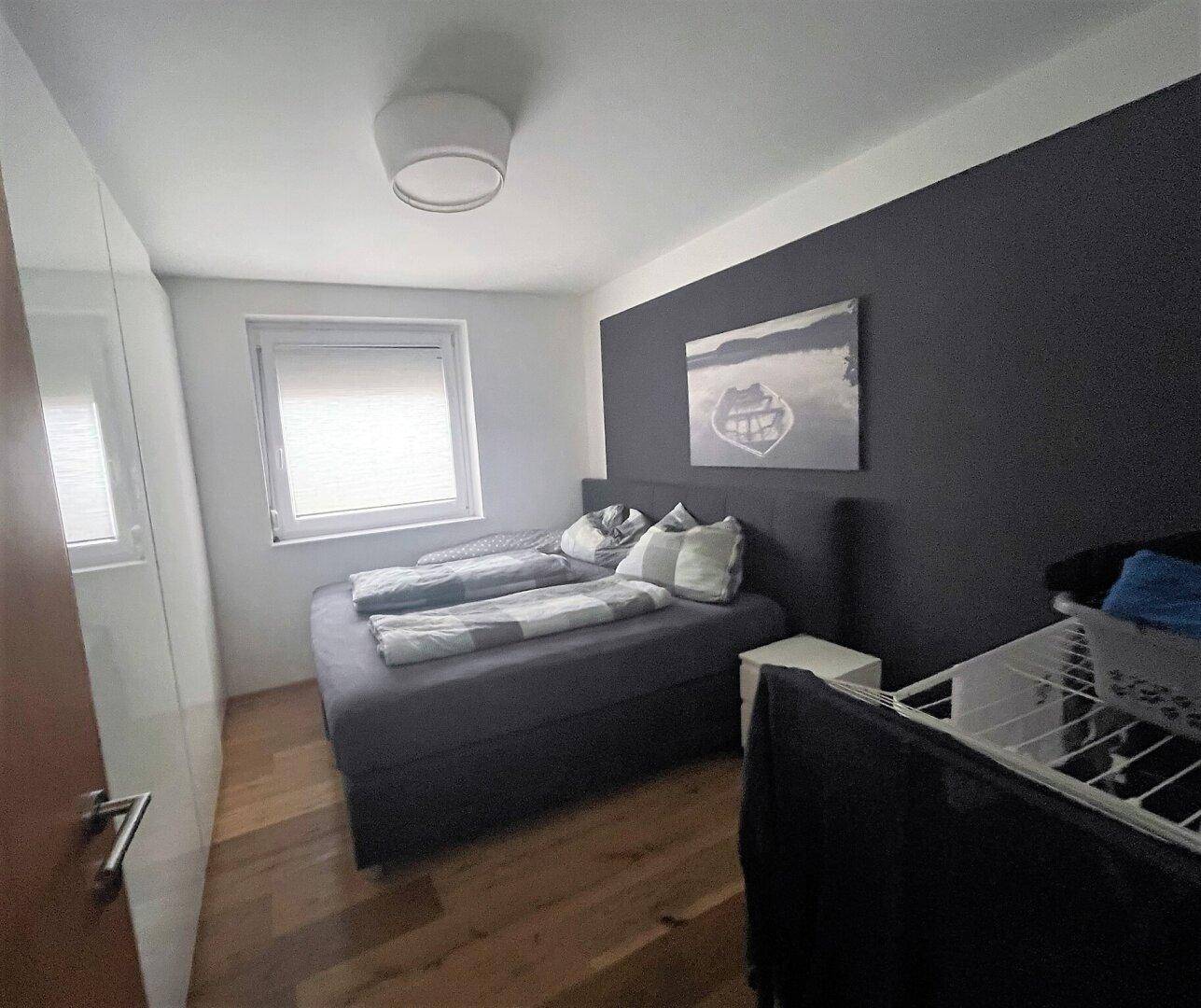 Gemütliches Schlafzimmer mit Doppelbett, dunkler Akzentwand und Holzboden, gut beleuchtet durch ein Fenster.