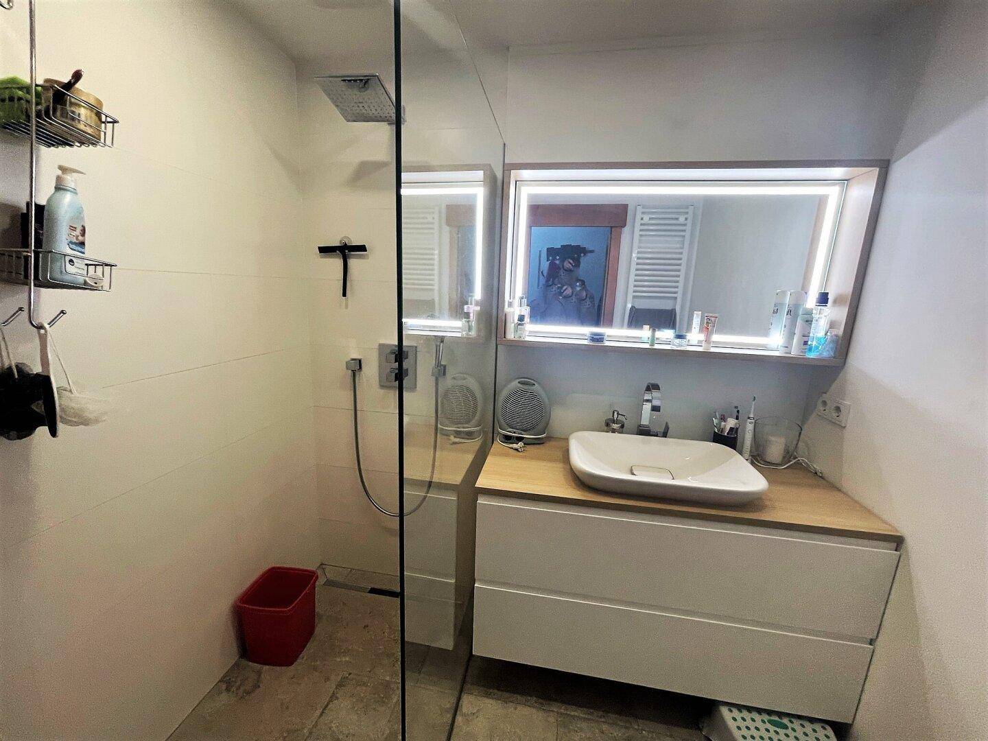 Modernes Badezimmer mit ebenerdiger Dusche, Einzelwaschbecken auf Holzunterschrank und beleuchtetem Spiegelschrank.