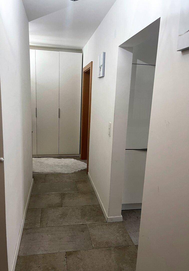 Langer, heller Flur mit Fliesenboden und weißen Wänden, der zu weiteren Räumen der Wohnung führt.