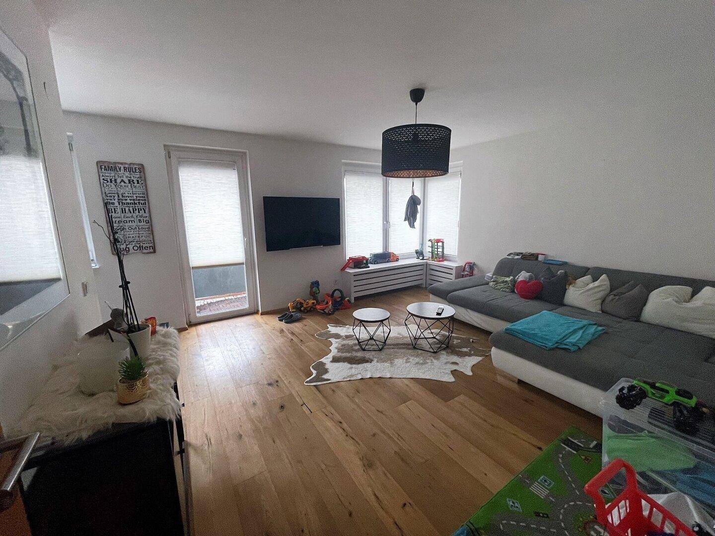 Helles Wohnzimmer mit großem Ecksofa, Holzboden und Zugang zu einem Außenbereich durch eine Fenstertür.