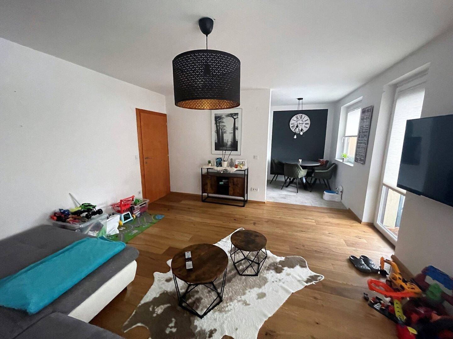 Heller Wohn- und Essbereich mit Holzboden, modernen Möbeln und einem Übergang zum Essbereich mit dunkler Wand.