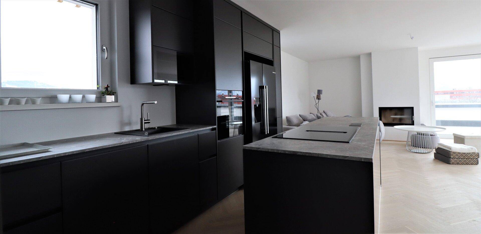 Elegante schwarze Einbauküche mit Induktionskochfeld, Spüle und Fensterblick.